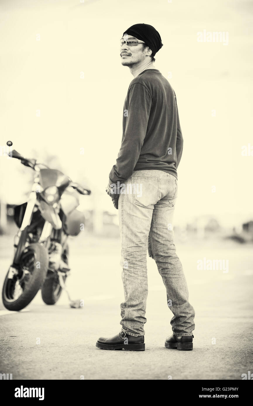 portrait of man biker standing on road with motorcycle in sunset, vintage style Stock Photo