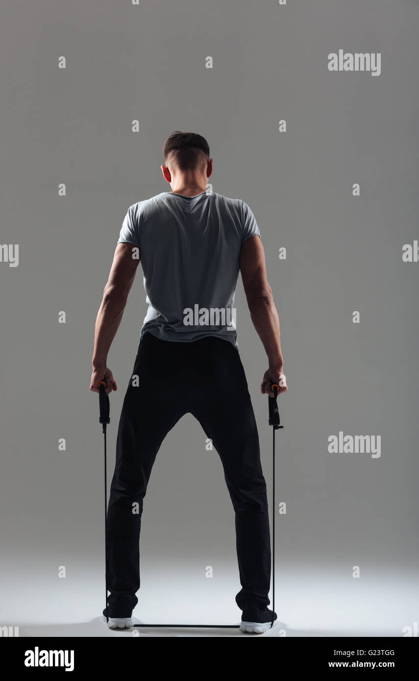 Rear view portrait of a fitness man workout with expander over gray background Stock Photo