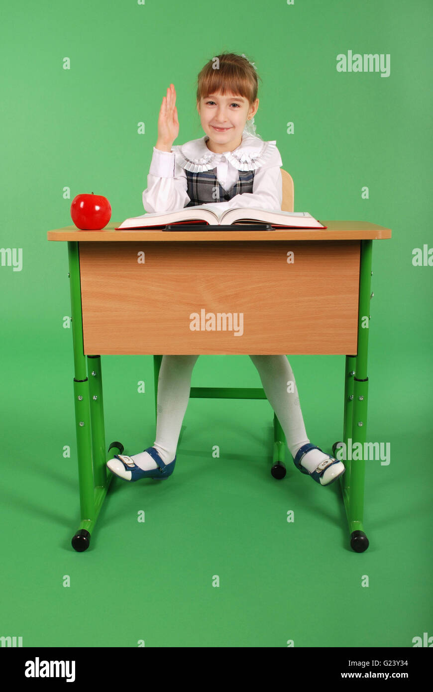 Girl in a school uniform sitting at a desk isolated on green background ...