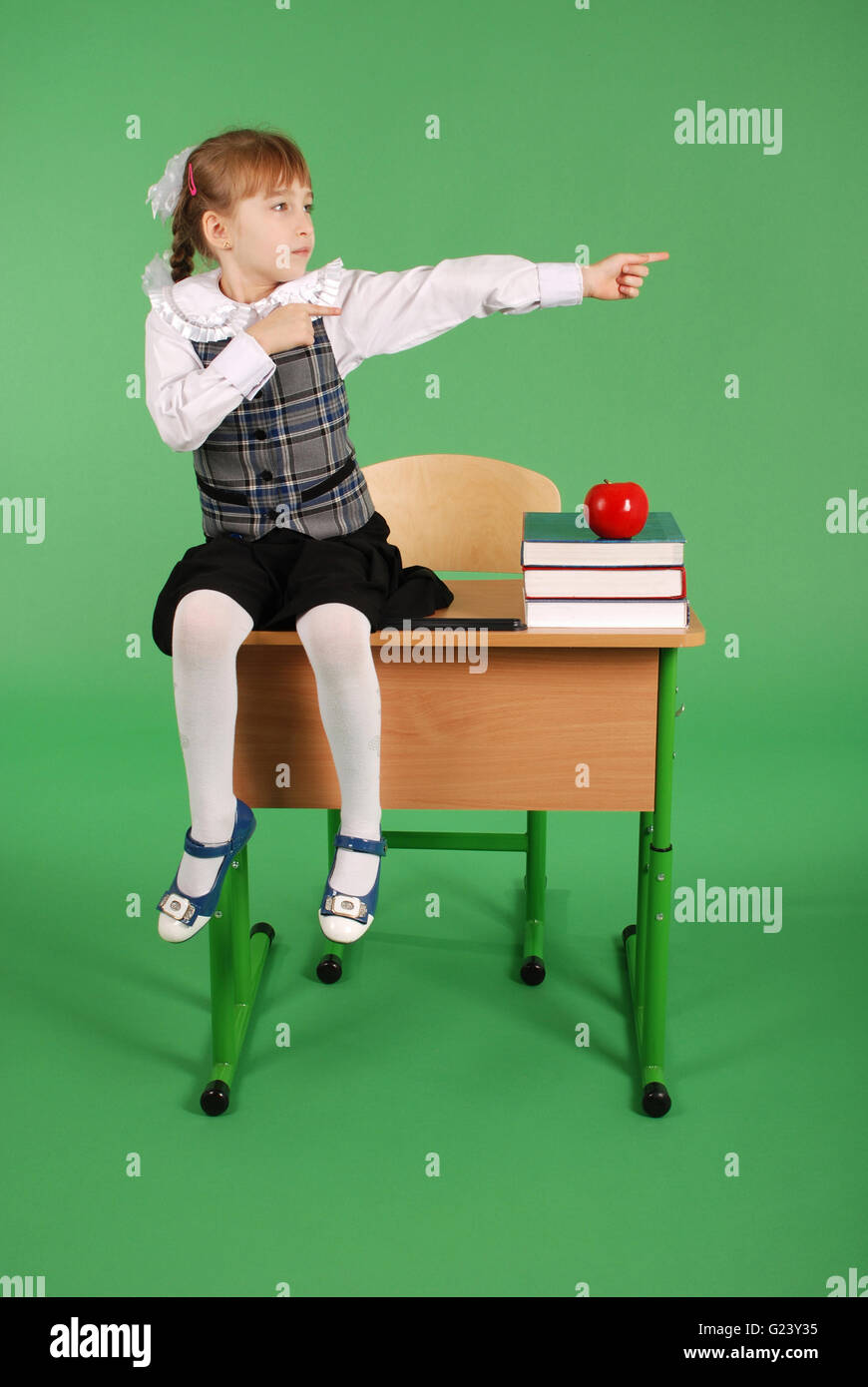 Girl in school uniform sitting on the desk isolated on a green