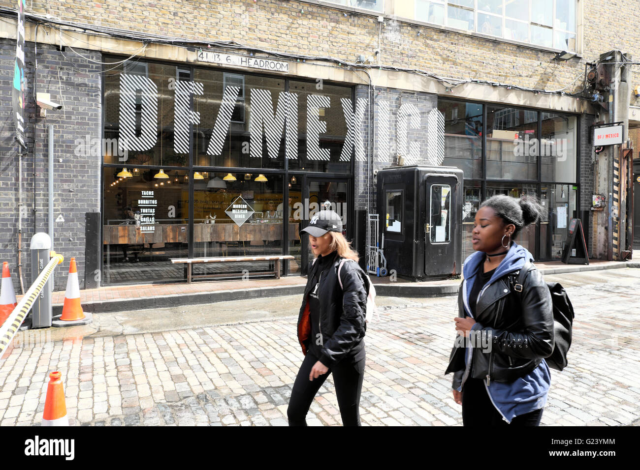 Young women walking past DF/Mexico Mexican restaurant on Dray Walk and Hanbury Street near Brick Lane in East London UK  KATHY DEWITT Stock Photo
