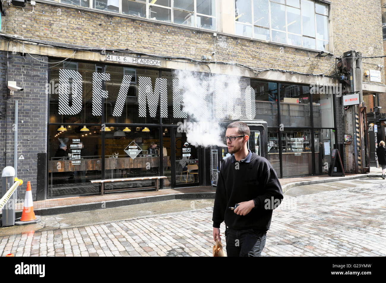 Man person vaping walking by DF/Mexico Mexican restaurant on Dray Walk & Hanbury Street near Brick Lane in East London UK  KATHY DEWITT Stock Photo