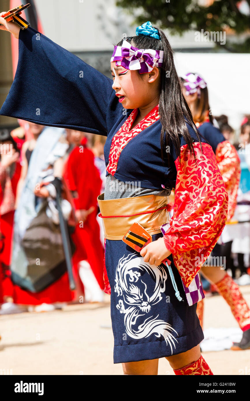 Japanese Hinokuni Yosakoi dance festival. Child, girl, 10-12 year old, dancing in happi coat, outdoors while holding naruko, wooden clappers. Stock Photo