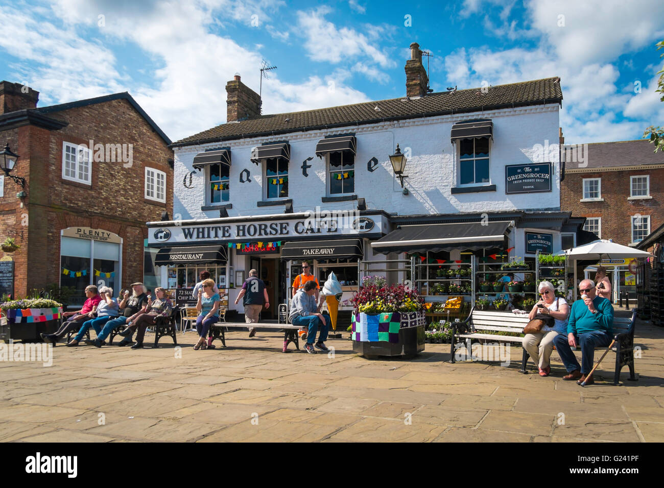People relaxing with ice creams outside the White Horse Café in Thirsk Market Place in the town centre on a warm spring day Stock Photo
