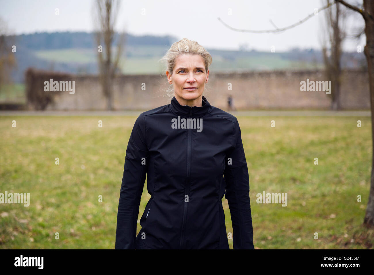 A medium shot of a middle aged female jogger standing in a park. Stock Photo