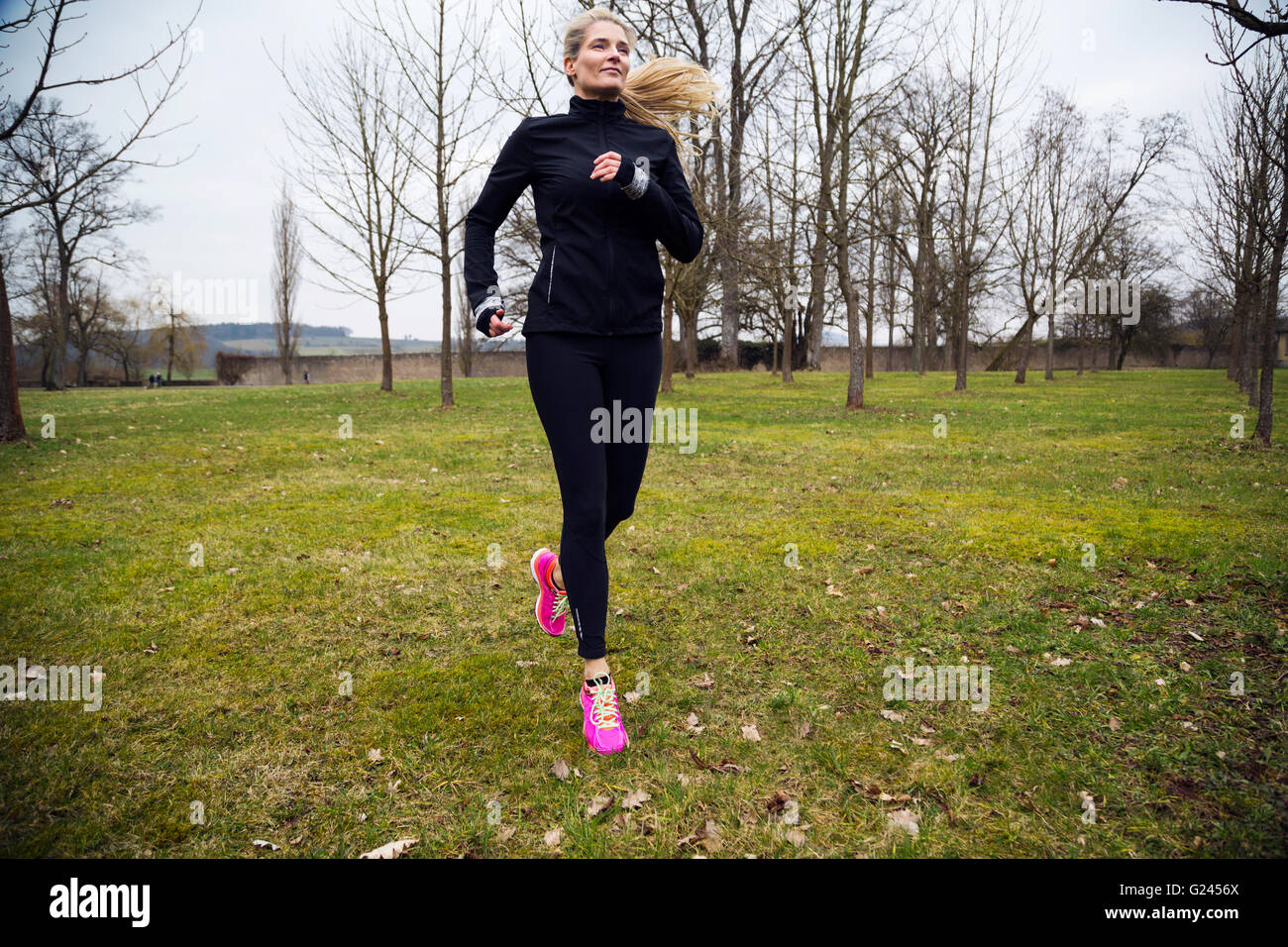 An attractive middle aged woman jogging in a park during winter. Long shot. Stock Photo