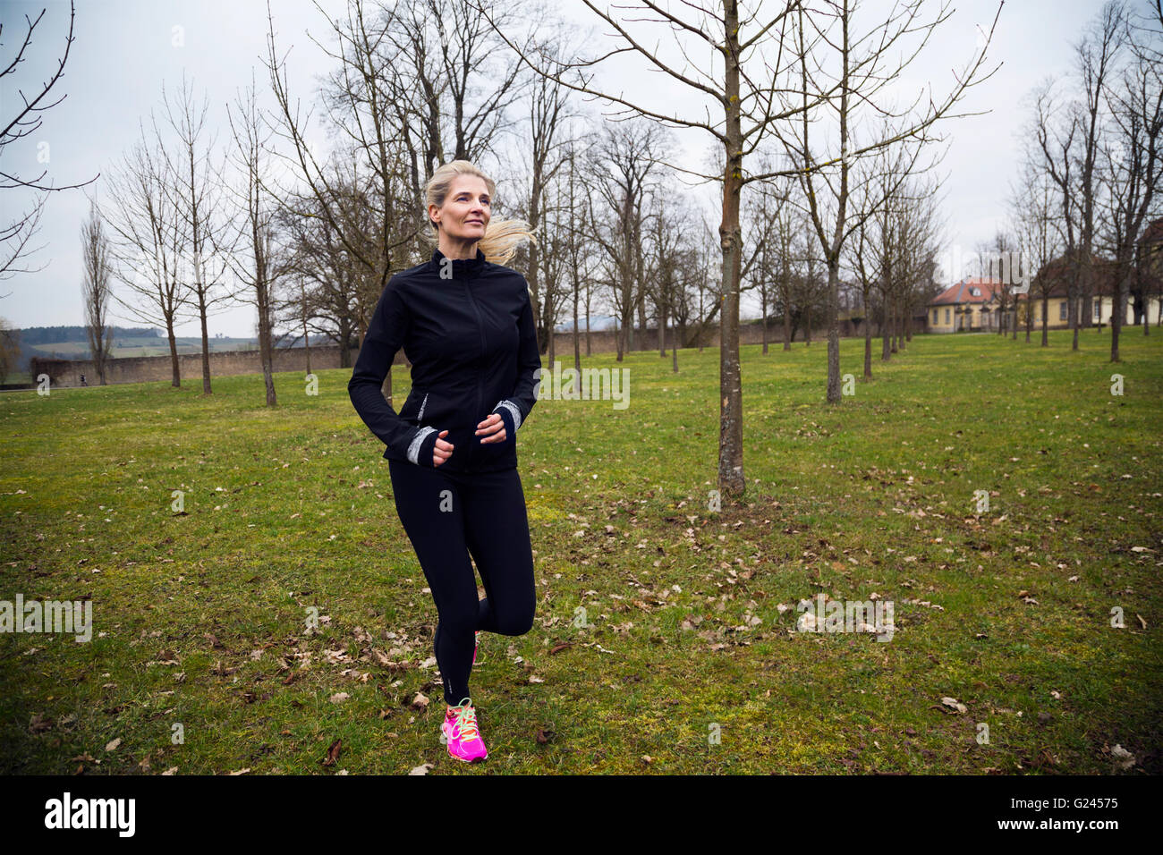 An attractive middle aged woman jogging in a park during winter. Long shot. Stock Photo