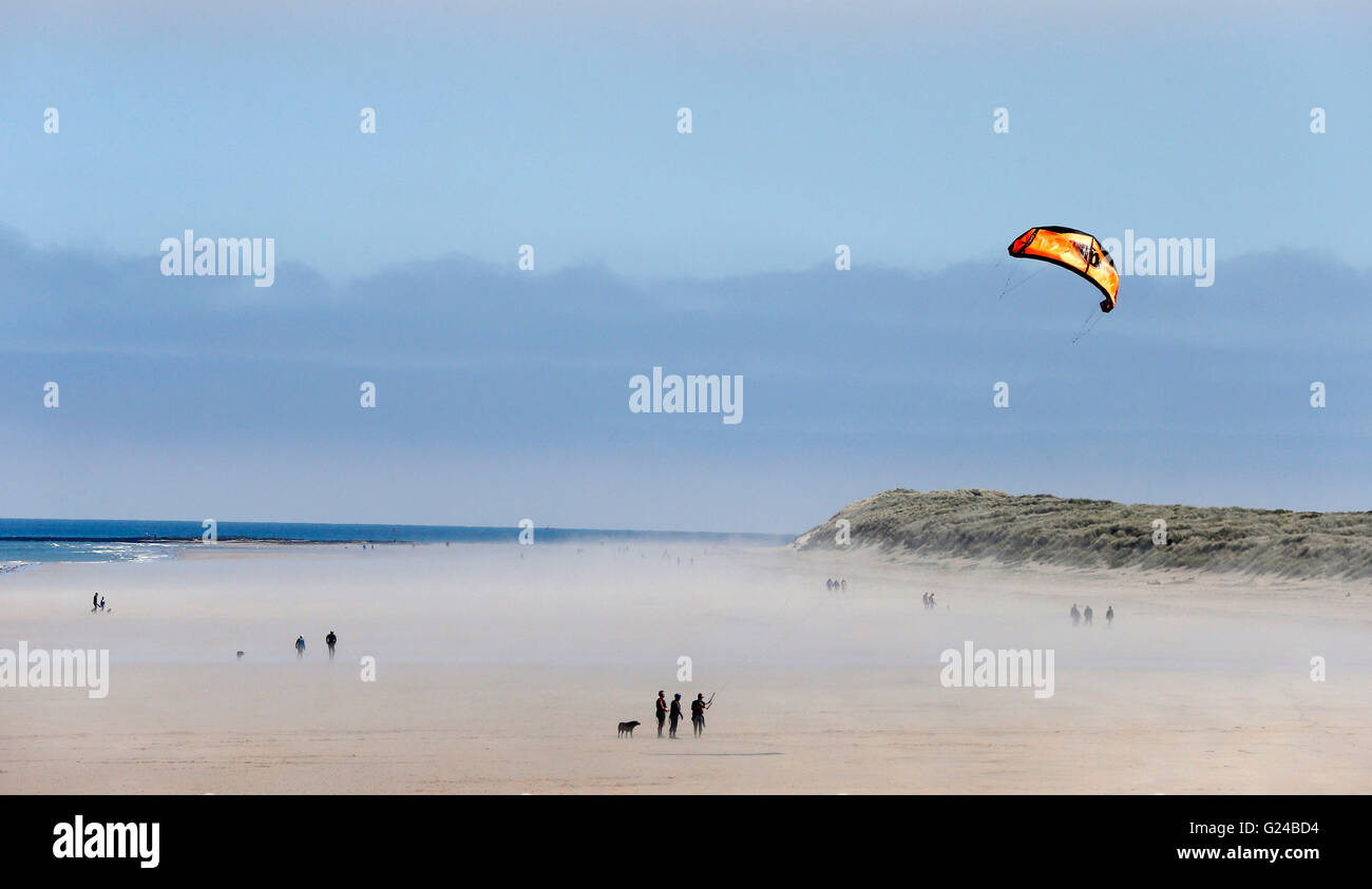 People walking and flying a kite enjoy the weather on Bamburgh beach, Northumberland as sea fret rolls in. Stock Photo