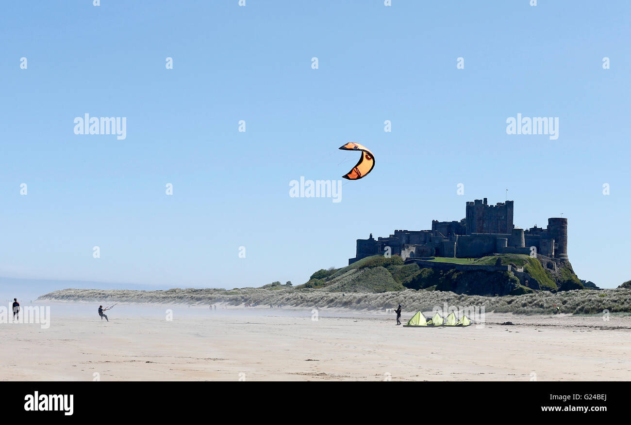 People flying a kite in front of Bamburgh Castle, enjoy the weather on Bamburgh beach, Northumberland as sea fret rolls in. Stock Photo