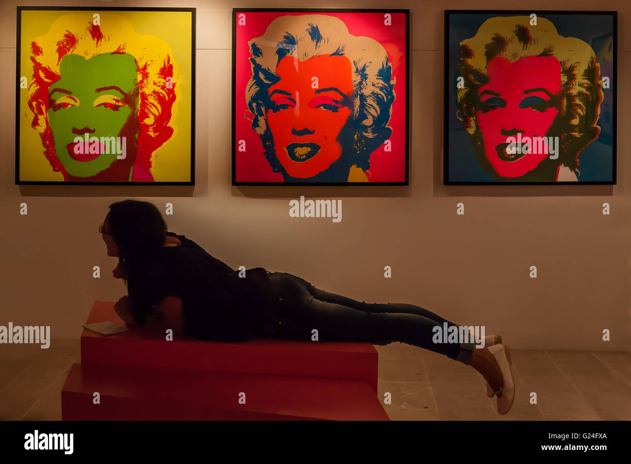 Andy Warhol exhibition, 'I Want to Be a Machine', in the Castello Aragonese, Otranto, Italy: a girl lies under 3 famous screenprints of Marilyn Monroe Stock Photo