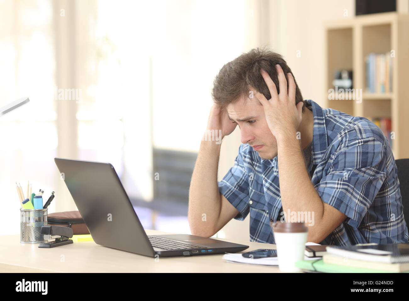 Worried and sad student male watching exam results on line in a laptop in a desk sitting at home room Stock Photo