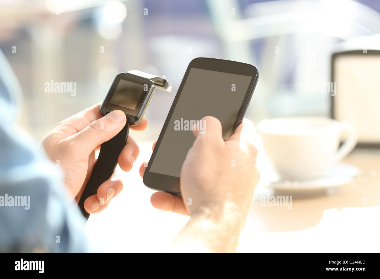 Close up of a casual man hands synchronizing a generic smartwatch and mobile phone in a bar terrace Stock Photo