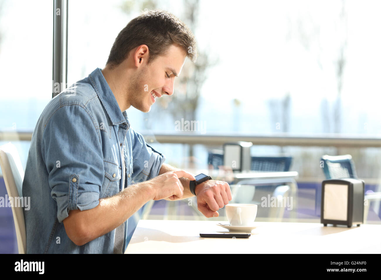 Profile of a man using a generic smartwatch with a mobile phone on line taking a break in a bar with drinks Stock Photo