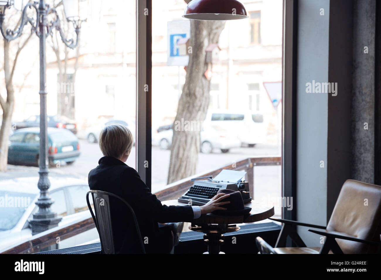 Blonde girl sitting backwards in a cafe and holding a hat Stock Photo