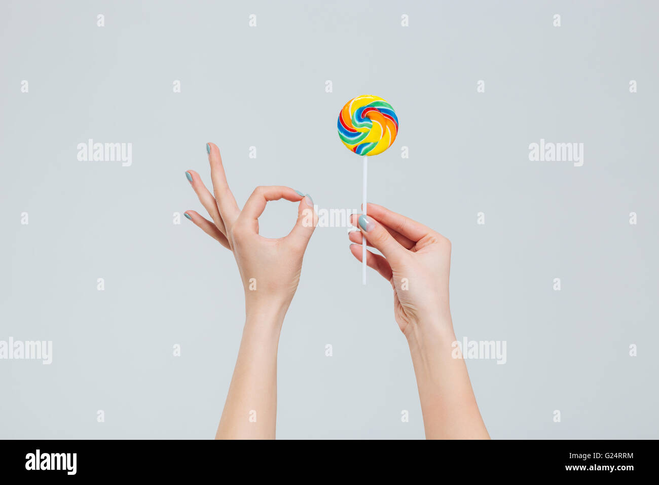 Coseup portrait of female hands holding lollipop and showing ok sign with fingers isolated on a white background Stock Photo