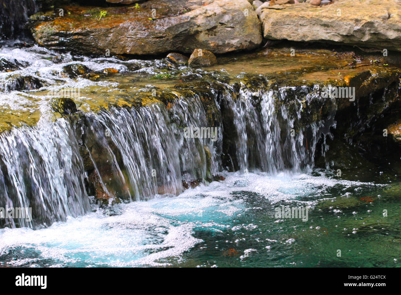 A garden pond supports a multi-tiered waterfall with many layers of rock slabs. Stock Photo