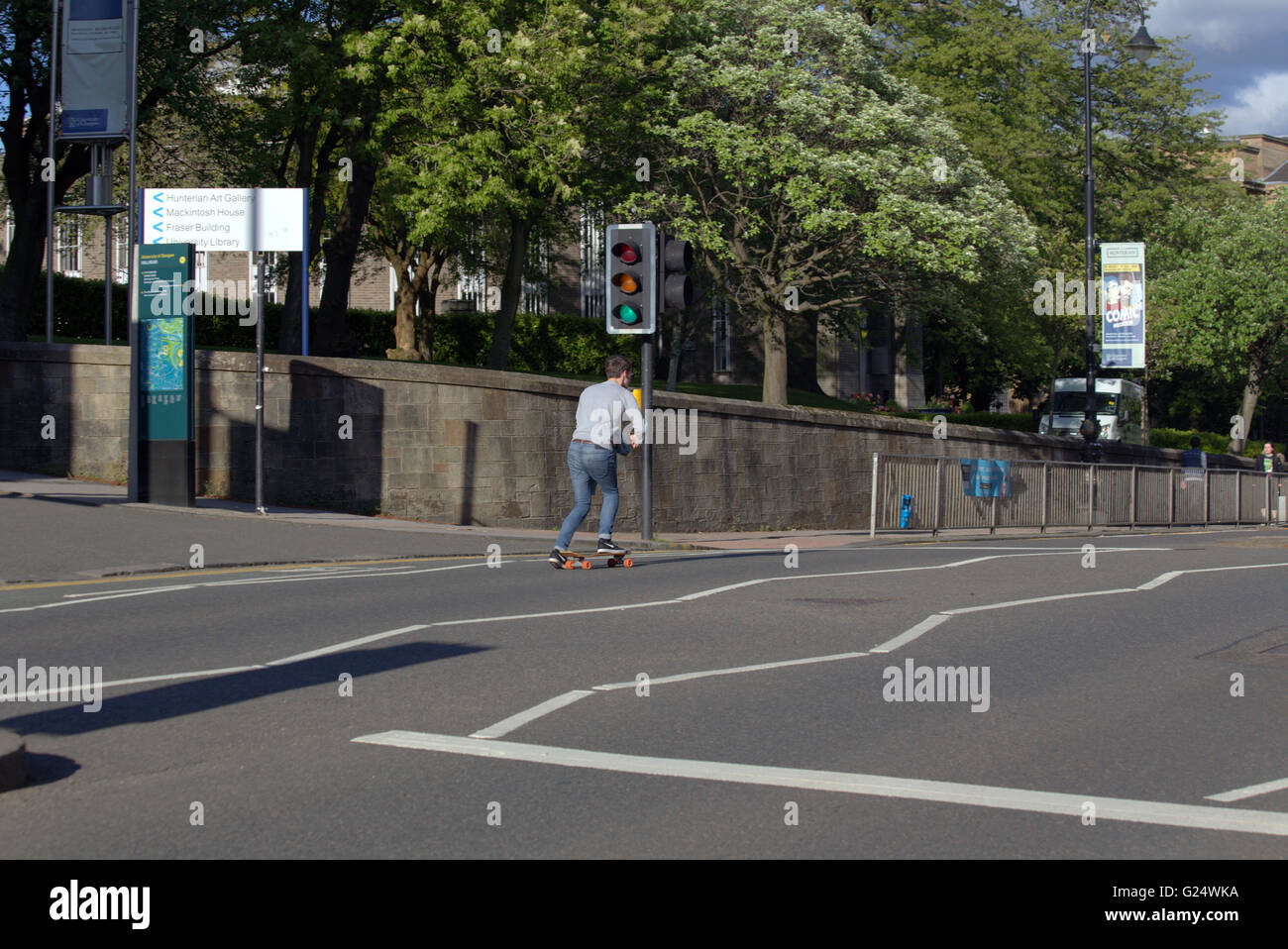Young man skateboarding down a street past traffic lights on green for go Glasgow, Scotland, UK. Stock Photo