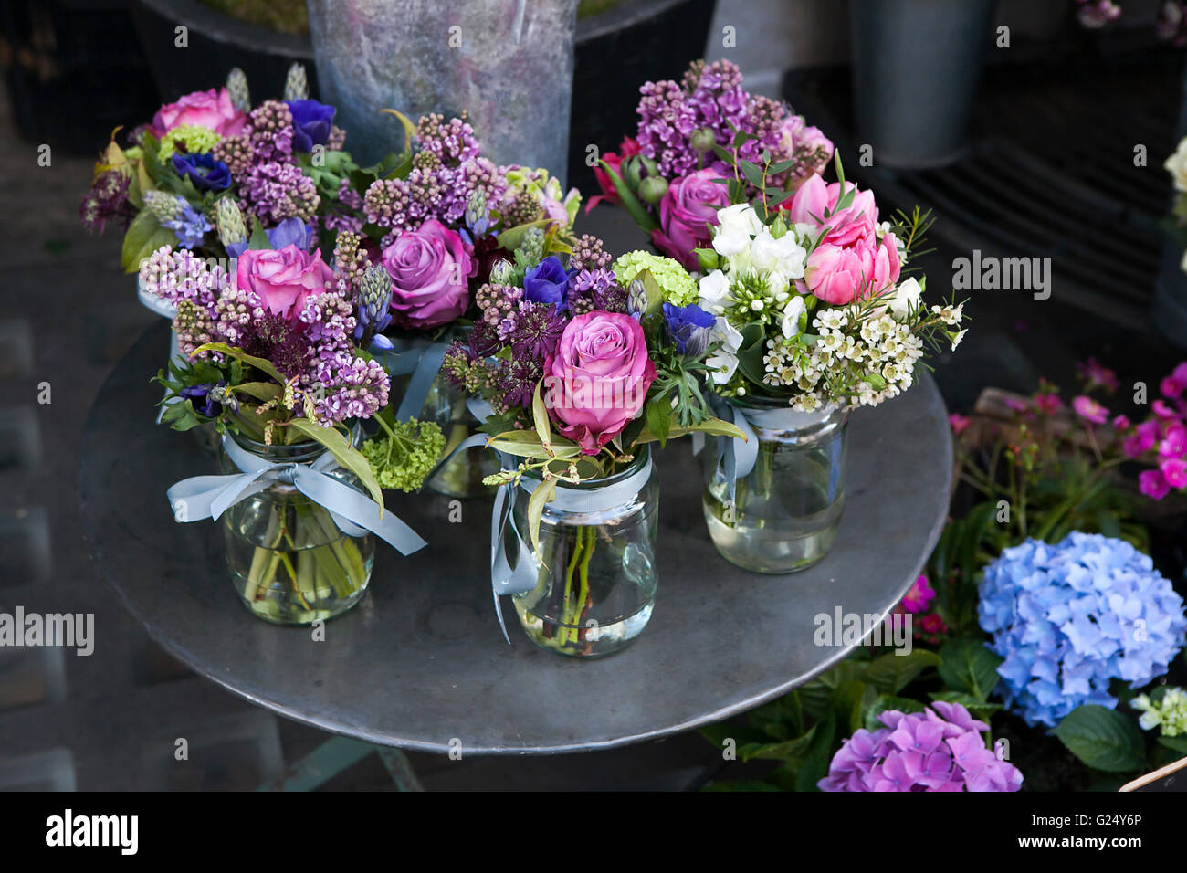 Small bouquets of lilacs, hyacinths, anemones, roses and peonies in small glass jars on an iron table. Stock Photo