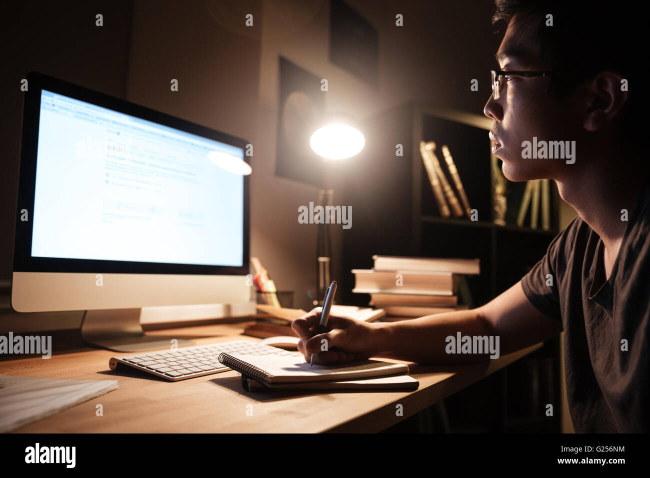 Profile of focused asian young man in glasses witing and studying using ...