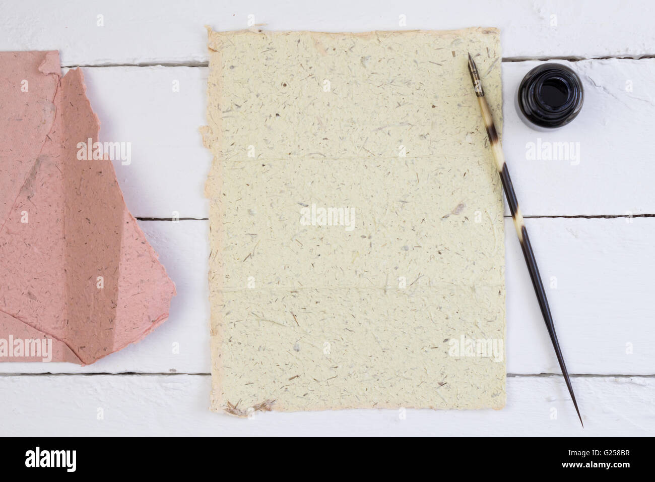 Top view of blank yellow paper, quill pen and ink on white deck table