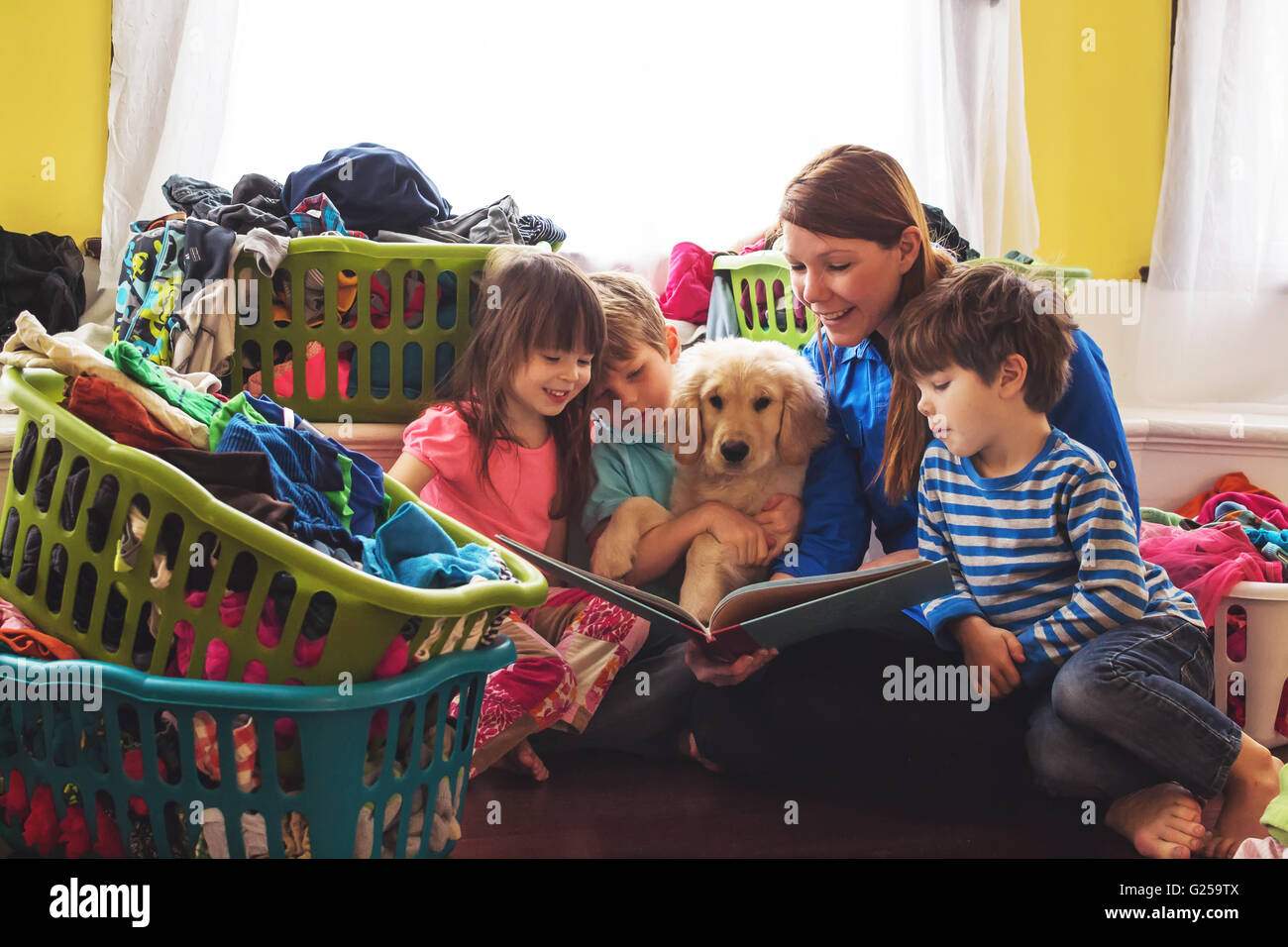 Smiling mother reading to three children and golden retriever puppy dog surrounded by laundry baskets Stock Photo