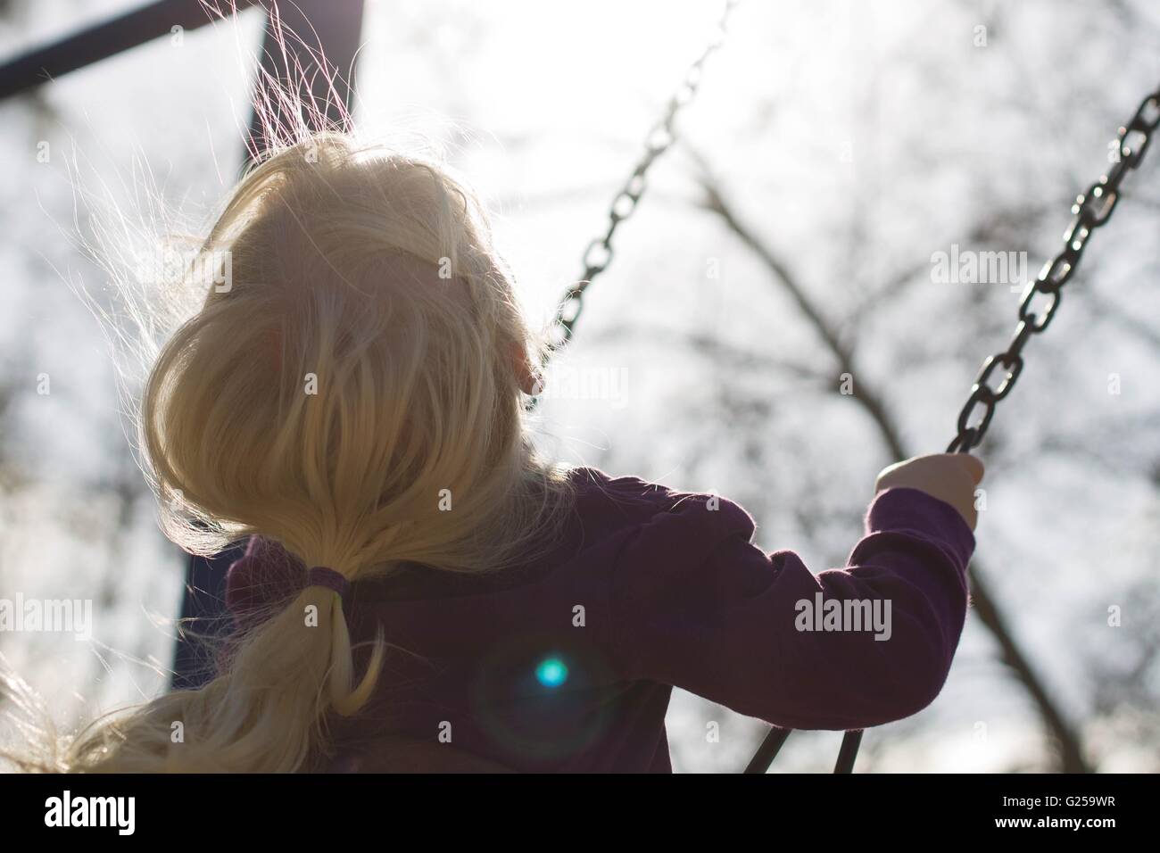 Rear view of a girl sitting on a swing Stock Photo - Alamy