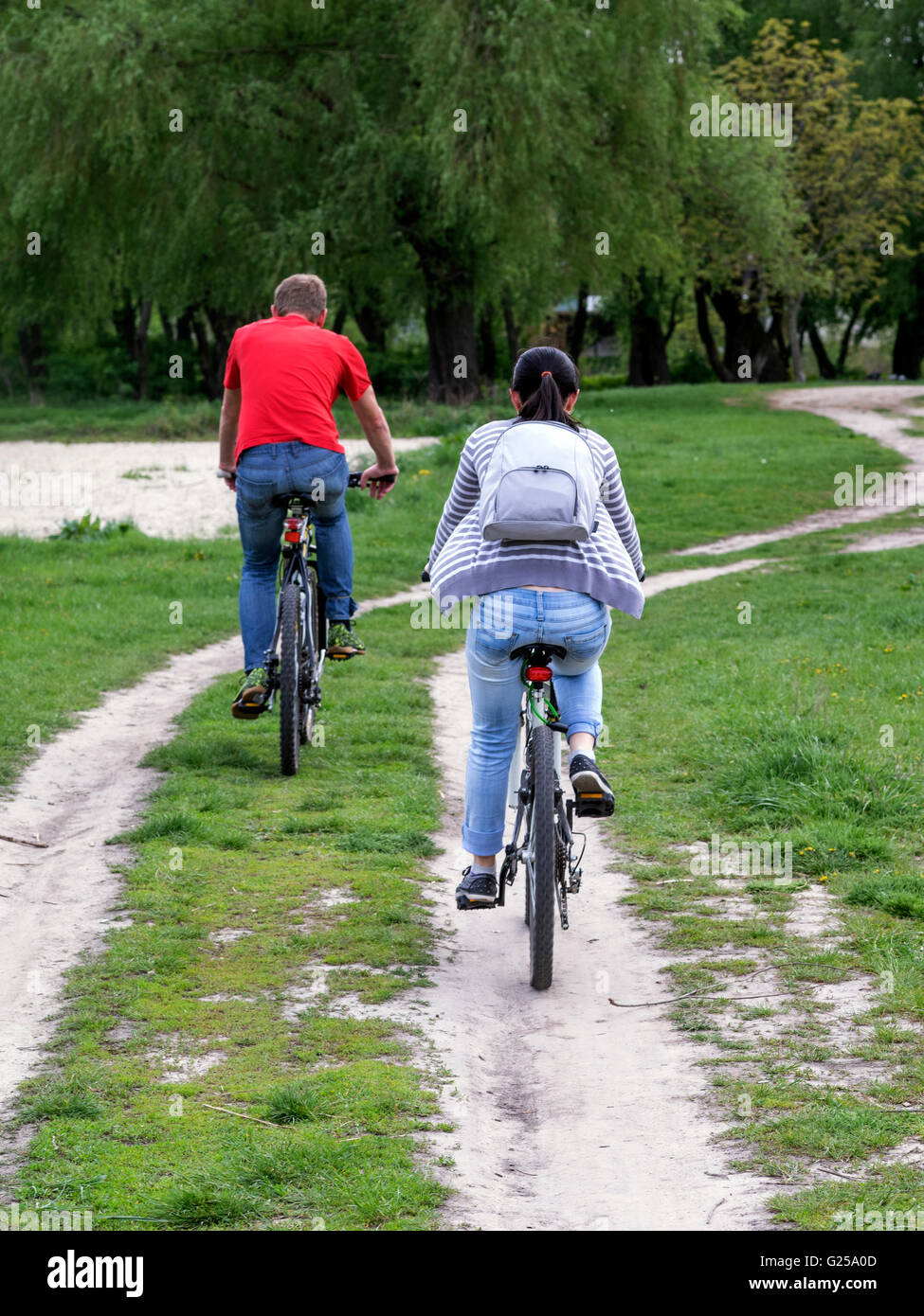 Couple cycling along road in rural countryside Stock Photo