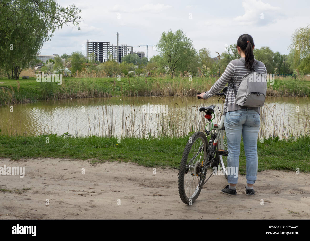 Woman standing with bike by lake looking at construction site Stock Photo