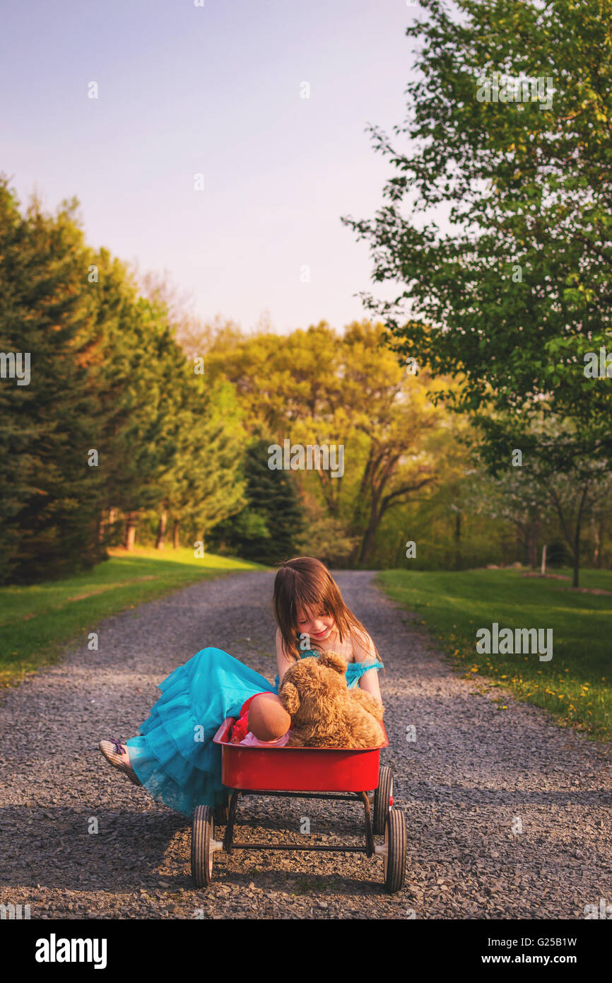 Girl sitting in wagon with doll and teddy bear Stock Photo - Alamy