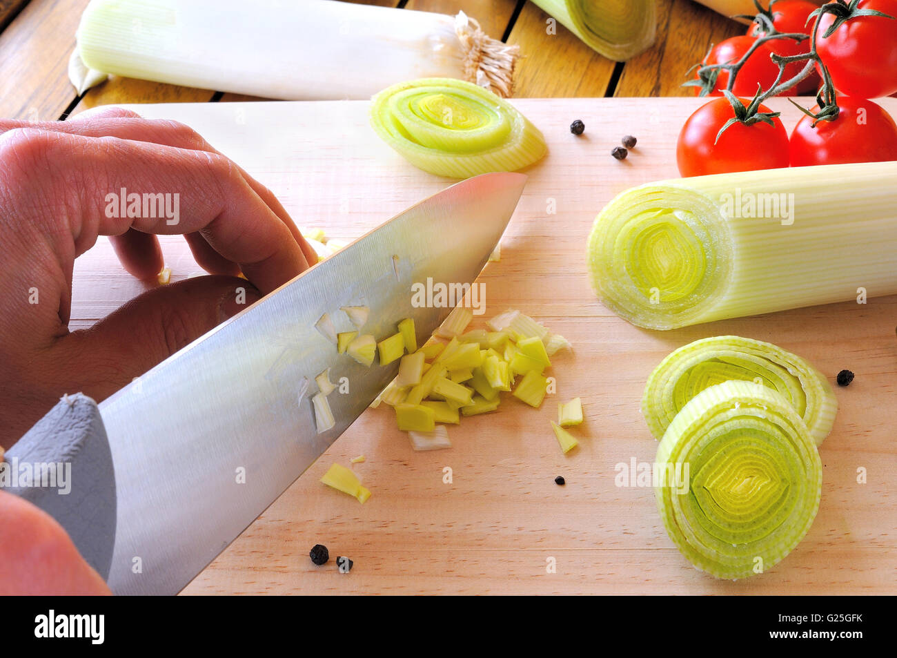 Chef cutting a leek sliced and diced on the cutting board on a kitchen table Stock Photo