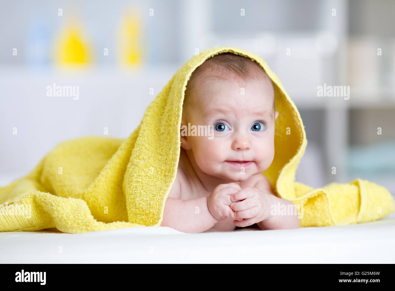 Funny baby under soft towel. Cute child lying on bed after bathing in living room Stock Photo