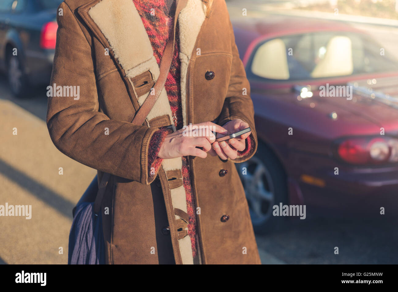 A young woman is standing by her fancy car and is using her smart phone in winter Stock Photo