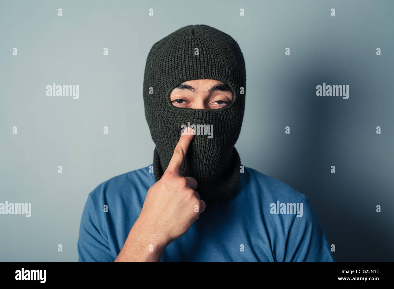 A stupid man wearing a balaclava is trying to pick his nose Stock Photo