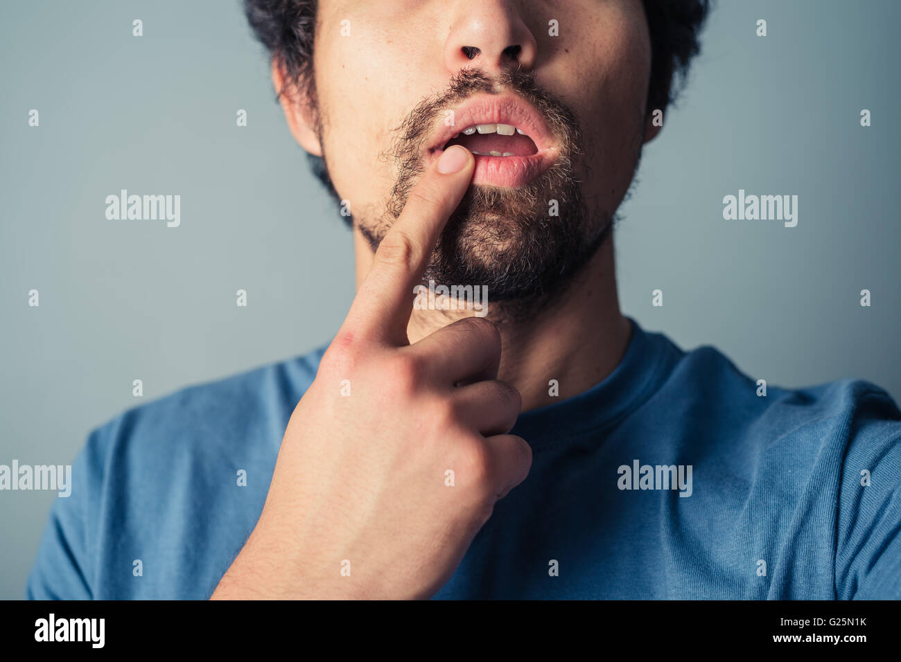 Confused young man touching his lip with his finger Stock Photo