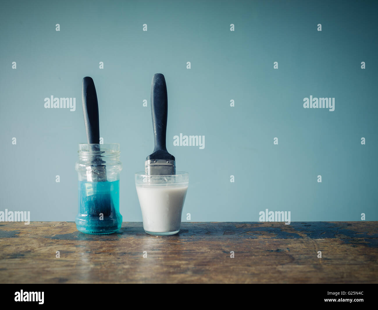 Two paintbrushes are soaking in jars of water and are coloring the