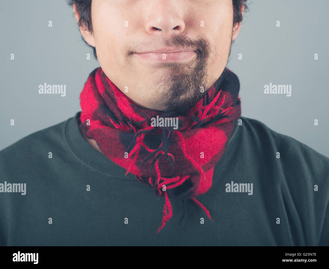 A young man with a half shaved beard is wearing a scarf Stock Photo