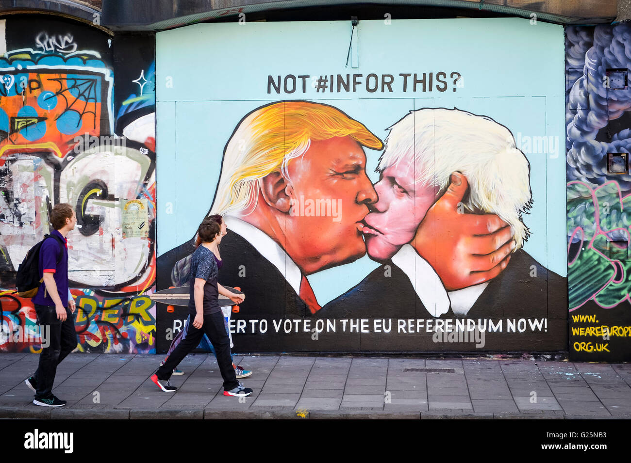 People walk past a graffiti mural of Donald Trump and Boris Johnson kissing, which is sprayed on a disused building in the Stokes Croft area of Bristol. Stock Photo