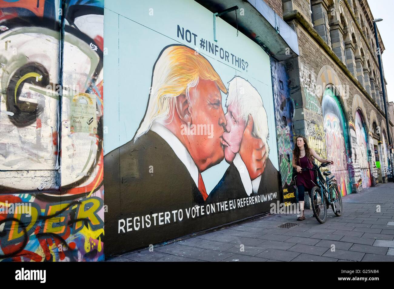 A woman walks past a graffiti mural of Donald Trump and Boris Johnson kissing, which is sprayed on a disused building in the Stokes Croft area of Bristol. Stock Photo