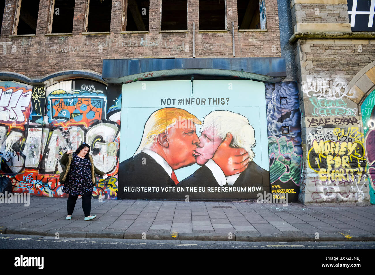 A woman walks past a graffiti mural of Donald Trump and Boris Johnson kissing, which is sprayed on a disused building in the Stokes Croft area of Bristol. Stock Photo