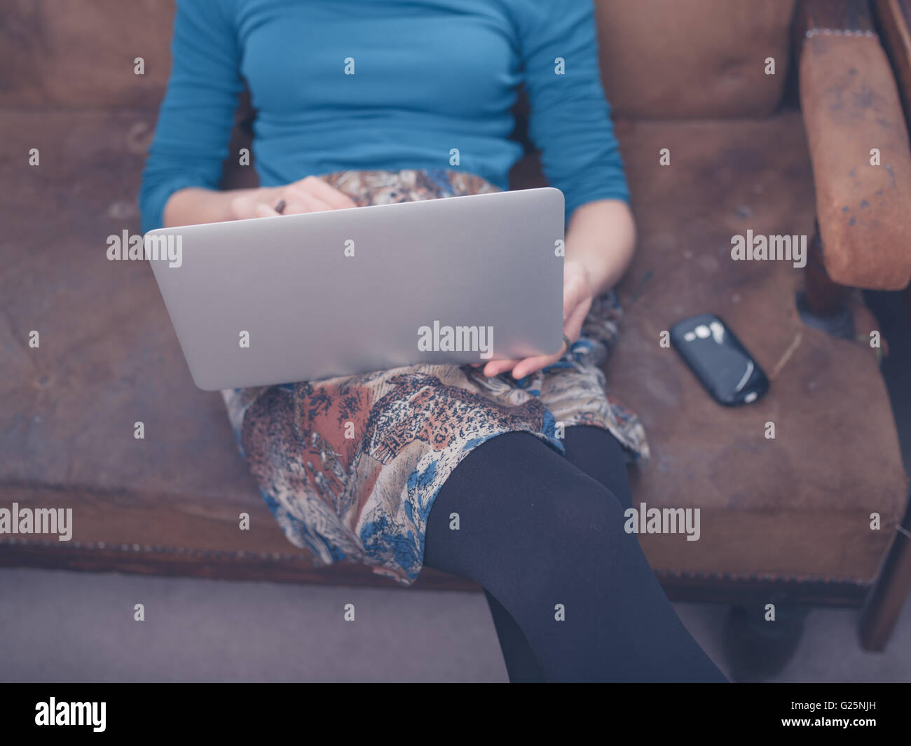 A young woman is sitting on a sofa at home in her living room and is ...