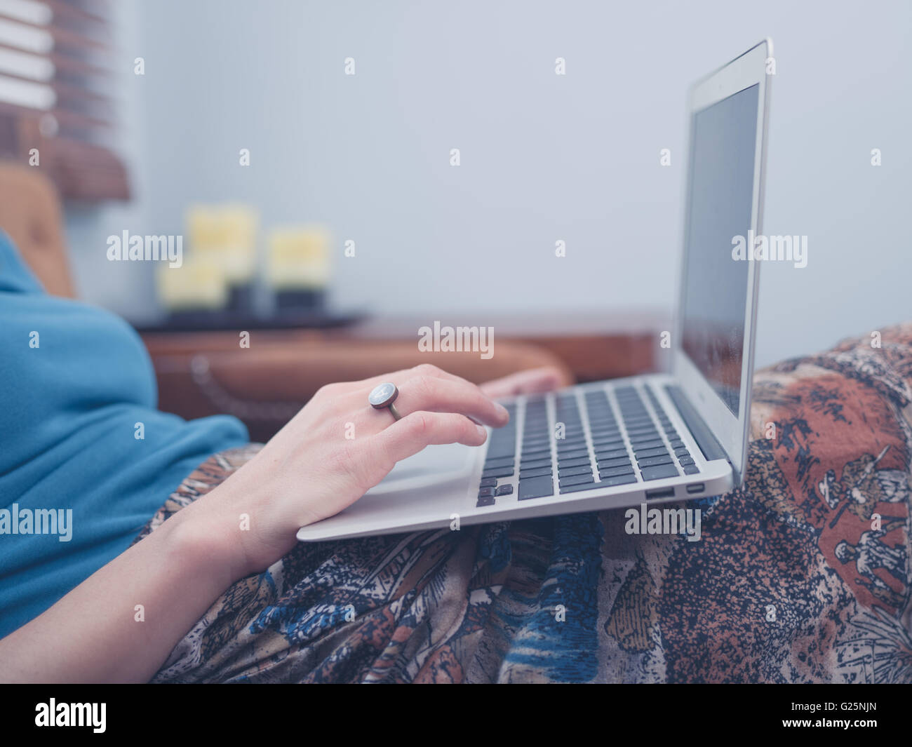 A young woman is sitting on a sofa at home in her living room and is ...