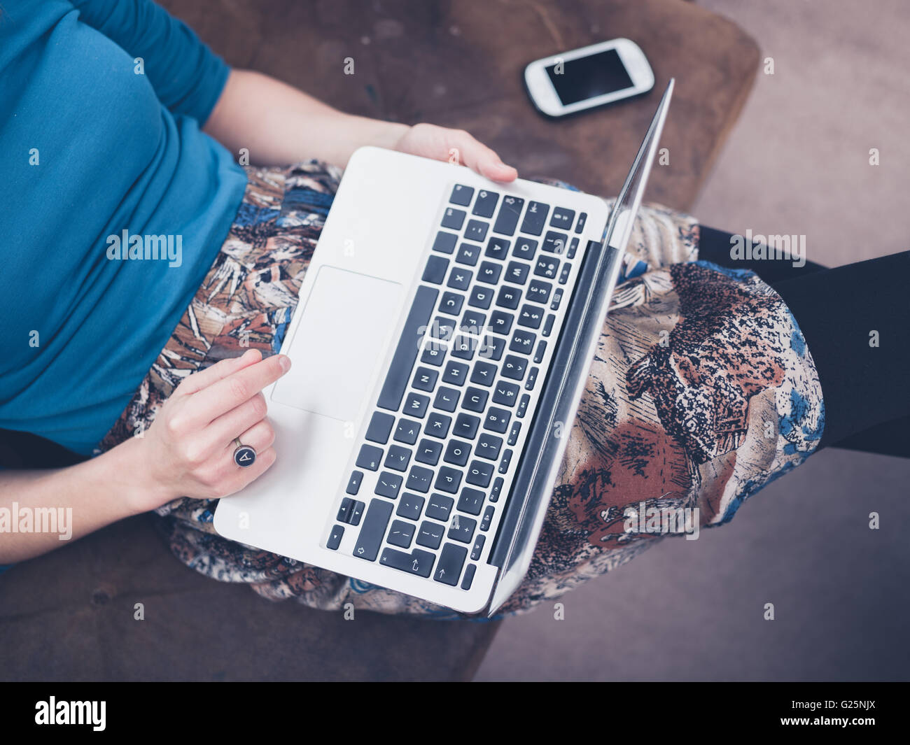 A young woman is sitting on a sofa at home in her living room and is ...