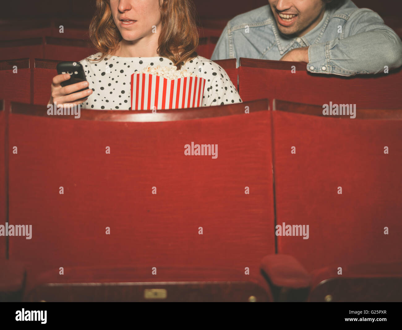 A young woman is using her phone in a movie theater with a man sitting
