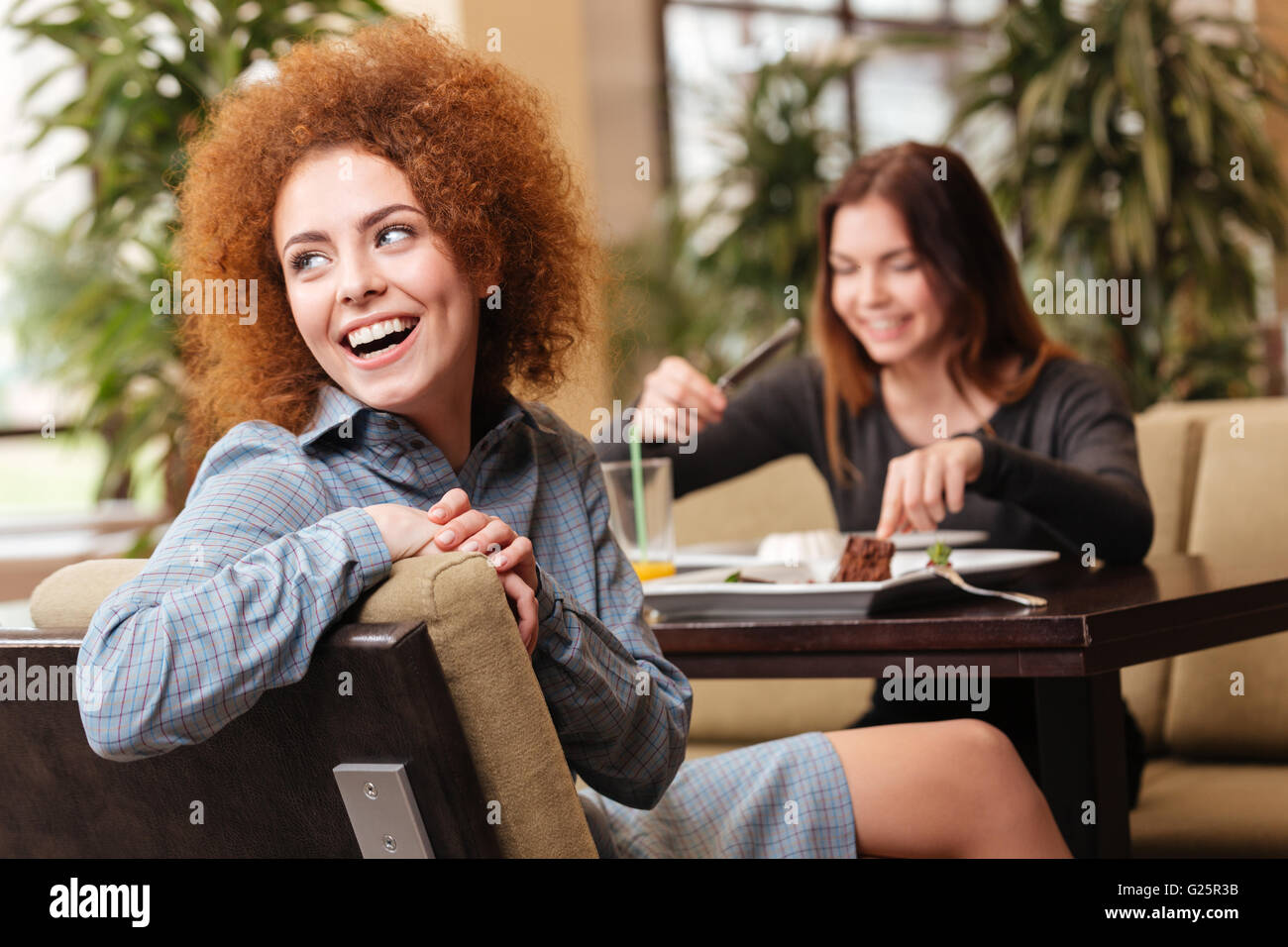 Two cheerful beautiful young women sitting in cafe and laughing together Stock Photo