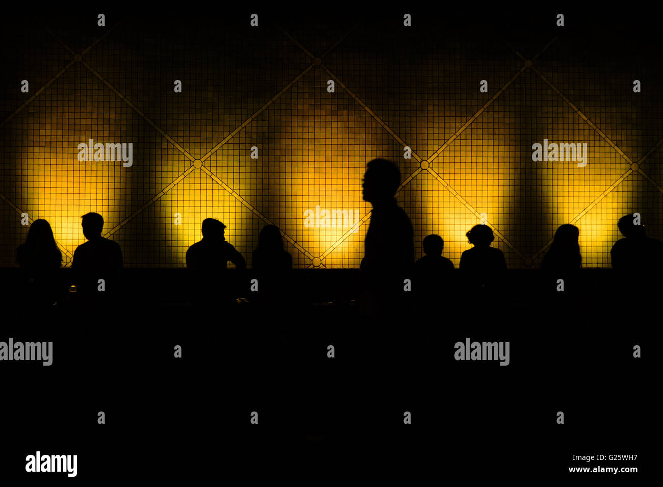 Silhouettes of people sitting in front of a wall lighted with colored spots Stock Photo