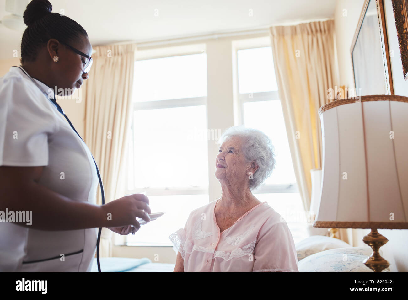 Female care worker nurse assists an elderly female patient with medicines for the day. Home caregiver giving medication dosage t Stock Photo