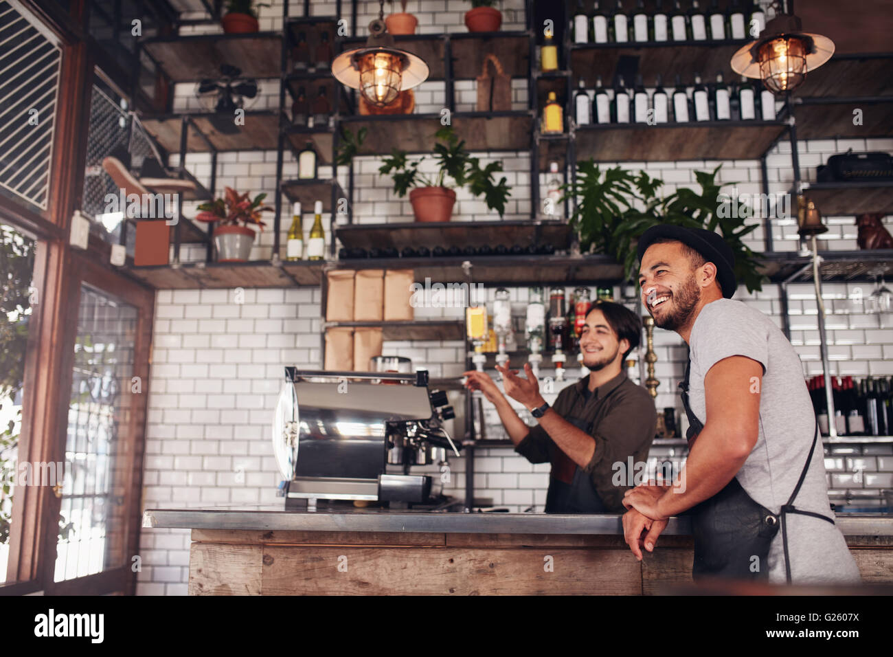 Coffee shop workers standing at the counter looking outside the cafe and smiling. Stock Photo