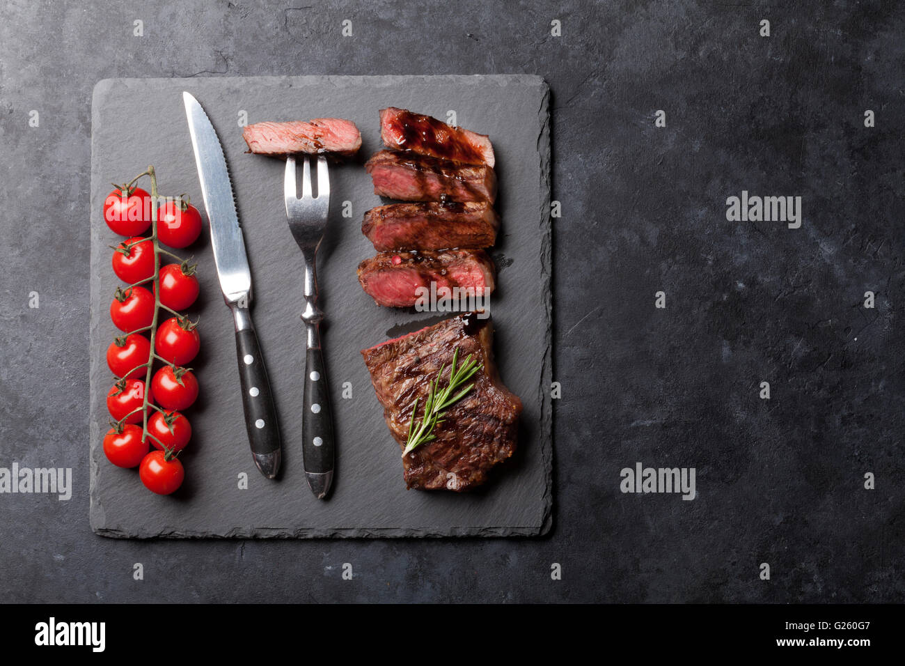 Grilled striploin sliced steak with salt and pepper over stone table. Top view with copy space Stock Photo