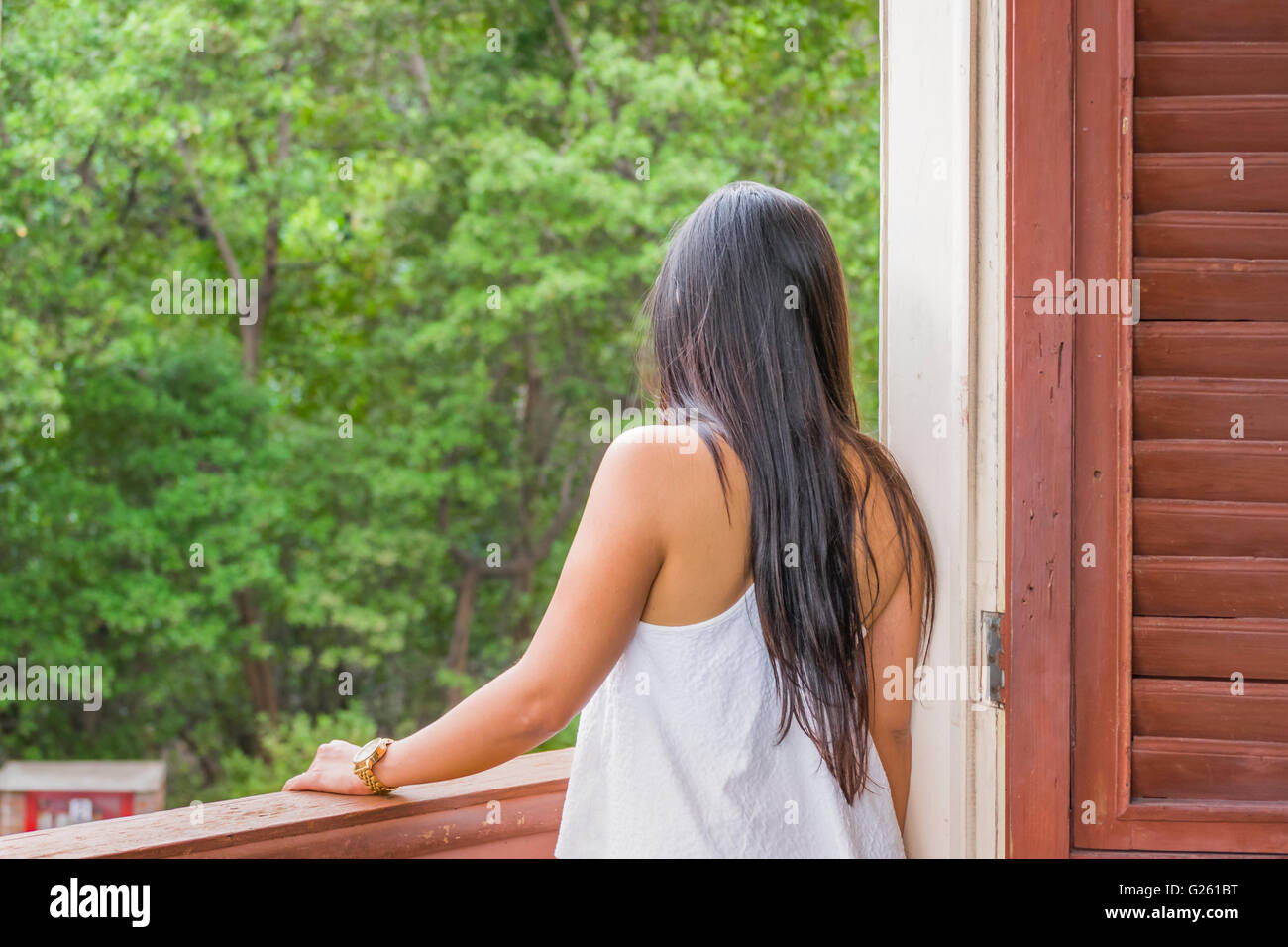 Back view of young adult woman elegantly dressed against forest background Stock Photo