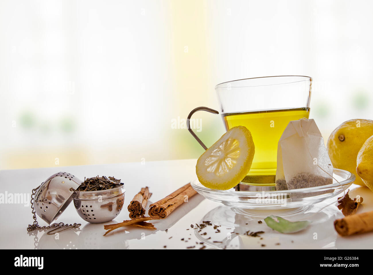 Glass cup green tea with cinnamon stick and lemon on a table in the living room. With teabag and metallic strainer Horizontal co Stock Photo